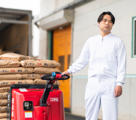 写真：縦に並べられた茶色い紙袋を機械で運んでいる男性職員